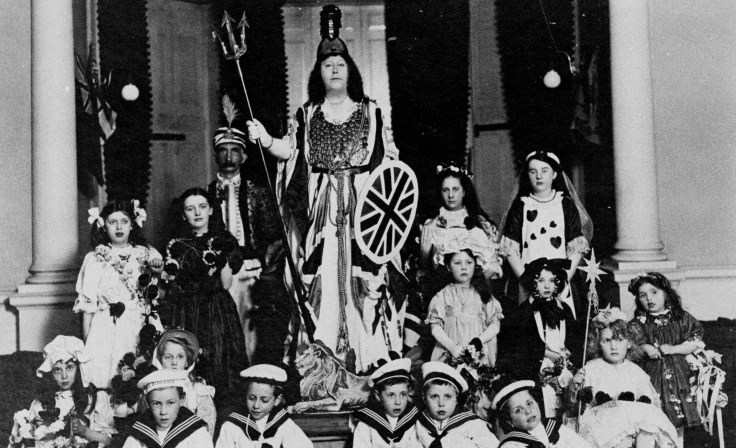 A group of children and young peopled dressed in costume, who are seated and stood in front of a woman in costume